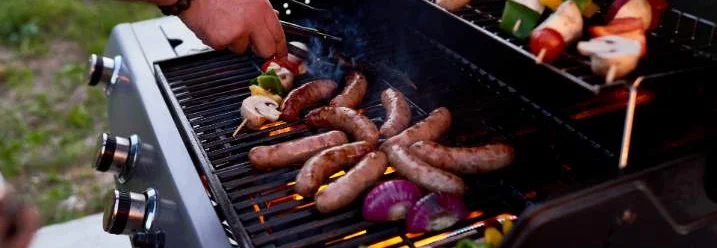 Person grillt Würstchen und Gemüse